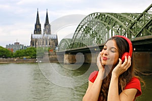 Portrait of young relaxed woman listening to music with urban background. City girl with red headphone enjoying music outdoors.
