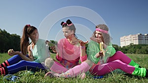 Portrait of young retro woman with chocolate bar sitting outdoors with friends disapproving eating healthful fruits