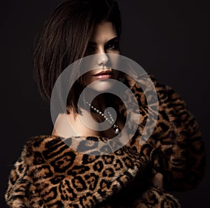 Portrait of young rich sexy brunette woman in leopard fur coat jacket with naked shoulders with expensive jewelry