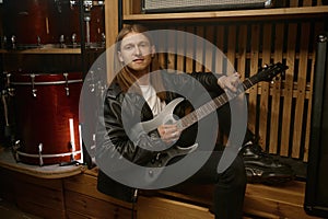 Portrait of young rock guitarist with musical instrument sitting on bench