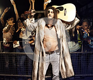 Portrait of young rock musician with guitar posing for excited audience at concert