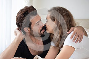 Portrait of young romantic couple hugging and kissing laying down on bed in morning. Man kiss girlfriend love, relationships,