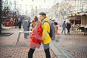 Portrait of young romantic couple in love kissing, hugging, walking on the street, wearning in bright down jackets