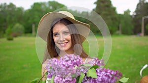 Portrait of young romantic smiling beautiful girl holding lilac in bouquet in nature forest outdoors looking at camera