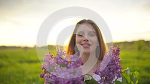 Portrait of young romantic smiling beautiful girl sniffing smelling lilac flowers in bouquet at sunset nature