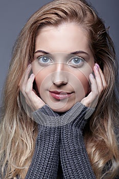 Portrait of young romantic woman in gray woolen sweater. Beautiful girl posing on grey studio background. Female with blonde hair