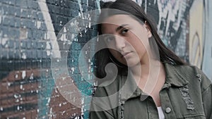 Portrait of a young sad brunette hipster girl with brown eyes near a wall with graffiti