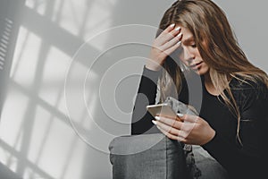 Portrait of a young sad crying girl with a smartphone in her hand.