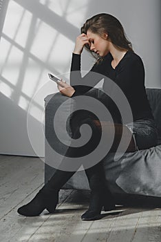 Portrait of a young sad crying girl with a smartphone in her hand.