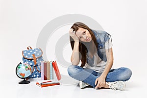 Portrait of young sad exhausted woman student in denim clothes resting forehead on hand, sit near globe backpack school