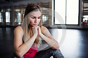 A portrait of young sad and frustrated girl or woman sitting in a gym.