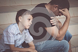 Portrait of young sad little boy and father sitting outdoors at the day time