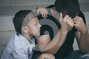 Portrait of young sad little boy and father sitting outdoors at the day time