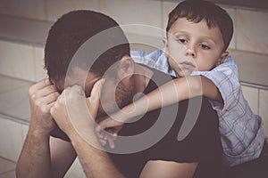 Portrait of young sad little boy and father sitting outdoors at the day time