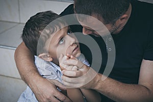 Portrait of young sad little boy and father sitting outdoors at the day time