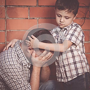 Portrait of young sad little boy and father sitting outdoors at the day time