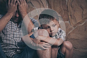 Portrait of young sad little boy and father sitting outdoors at the day time