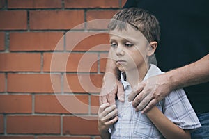 Portrait of young sad little boy and father standing outdoors at the day time