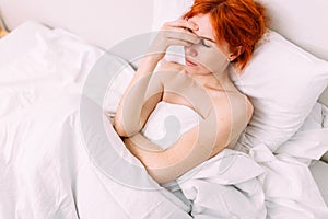 Portrait of a young sad tired woman lying in bed. Illness and headache