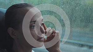 Portrait of young sad woman looking out the wet window, while travelling by bus.