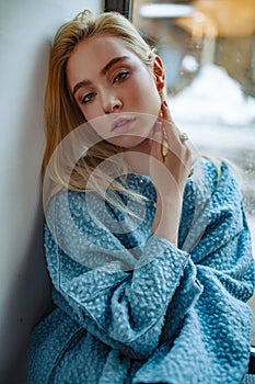 Portrait of young sad woman next to window.