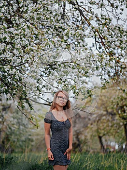 Portrait of a young school teacher with glasses in a spring green apple garden