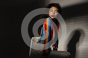 Portrait of a young seductive woman in colorful top. Image with shadows, posing with closed eyes.