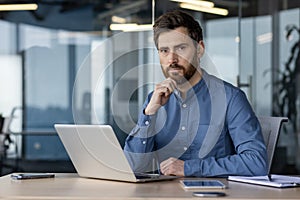 Portrait of a young serious businessman, lawyer and company founder sitting in the office at the desk and confidently