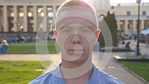 Portrait of young serious businessman in shirt looking into camera with cityscape at background. Close up of confident