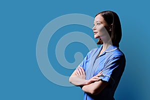 Portrait of young serious female nurse looking in profile on blue background