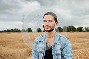 Portrait of young serious man in denim jacket in wheat field.