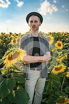 Portrait of a young serious stylish man in a hat in nature in a sunflower field
