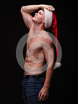 Shirtless Santa in a red hat on a black background. Handsome Christmas guy. New Year party concept.