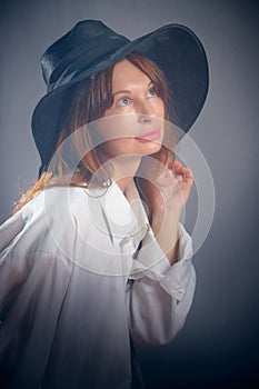 Portrait of a young sexy girl in a white shirt and hat on a grey background. Classic style. dramatic portrait
