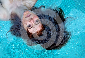 Portrait of young sexy redhead woman, swimming in the pool, the red hair under water, copy space