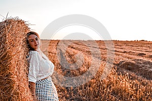 Portrait of young sexy woman on the haystack in morning sunlight, countryside. Beautiful woman in a dress sits on a