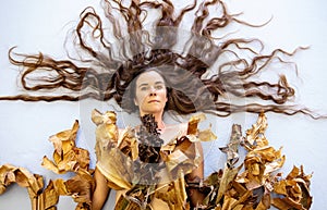 Portrait of a young sexy woman with long brown fan-shaped hair artfully decorated covered by leaves of dry decorative banana tree