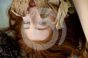 Portrait of a young sexy woman with red hair artfully covered between leaves of dry, withered banana tree