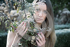 Portrait of young sexy woman standing in winter garden behind a rose bush with frost on leaves