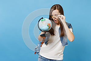 Portrait of young shocked concerned woman student with opened mouth with backpack removing glasses look on world globe