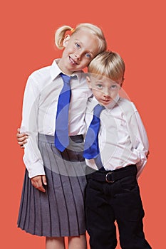 Portrait of young siblings in school uniform with arm around over orange background