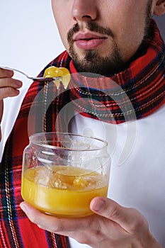 portrait of a young sick man in a scarf eating honey with a spoon