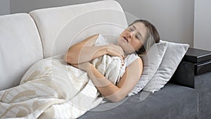 Portrait of young sick woman feeling unwell lying under blanket on sofa