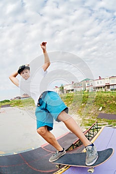 Portrait of a young skateboarder doing a trick on his skateboard on a halfpipe ramp in a skate park in the summer on a