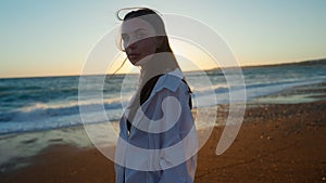 Portrait of young slim woman looking at camera standing at golden sunset on Mediterranean sea beach. Relaxed confident