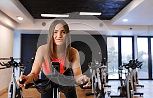 Portrait of young slim woman in sportwear workout on exercise bike in gym. Sport and wellness lifestyle concept