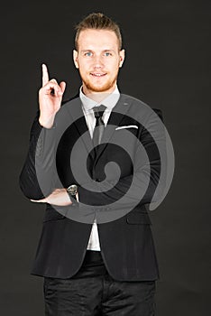 Portrait of young smart and handsome business man in black suit standing on isolated black background