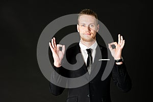 Portrait of young smart and handsome business man in black suit standing on isolated black background