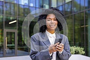 Portrait of a young smiling African American woman in a business suit standing outside an office building, holding a