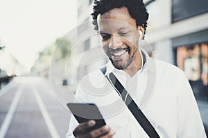 Portrait of young smiling african man using smartphone hands while standing at sunny city street.Concept of happy